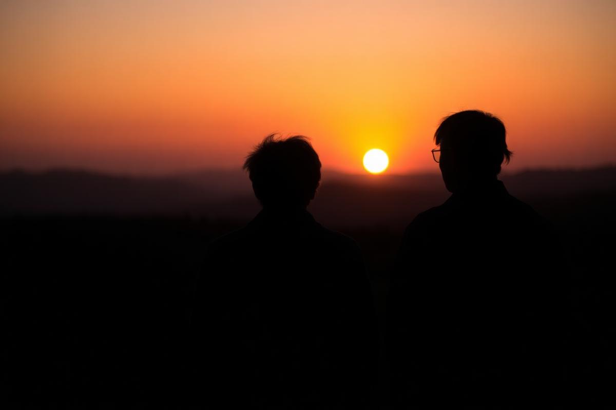 Silhouettes of two people of different ages watching a sunset together