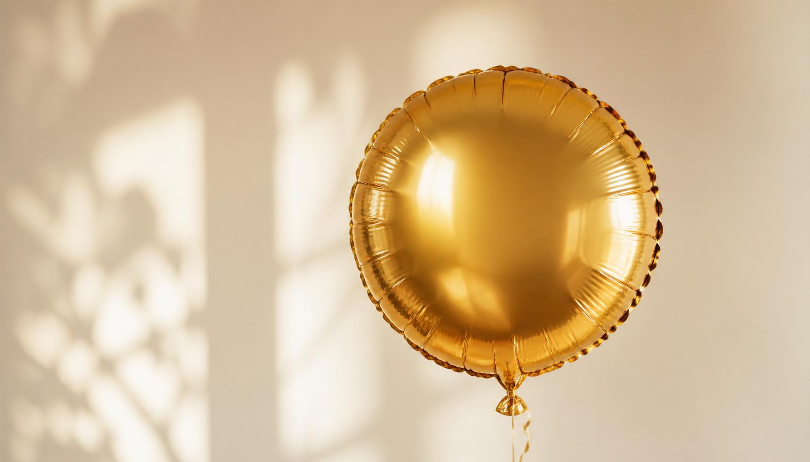 Single gold foil balloon against a soft cream background in warm afternoon light